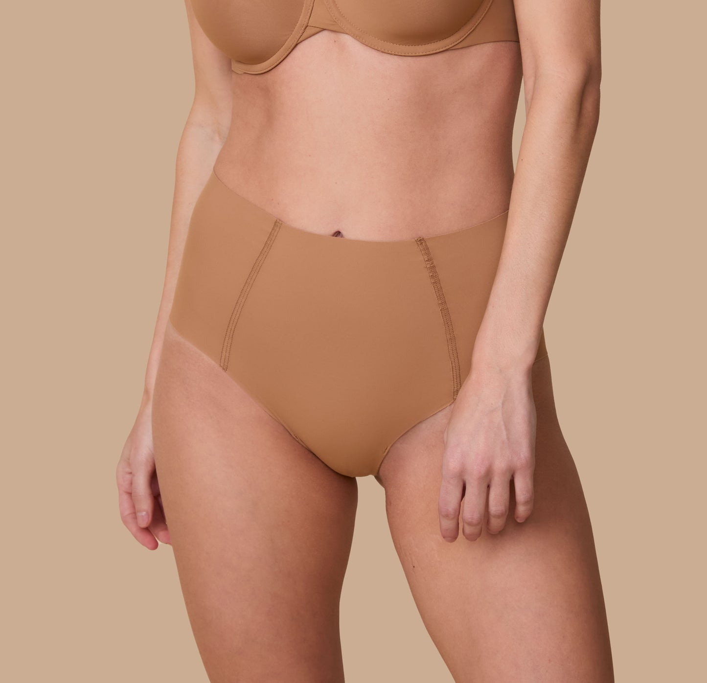 A close-up of Gracie wearing the No-Show Highwaist Brief in Tan. The seamless, high-waisted design offers a smooth, invisible fit under clothing. sizing: Gracie wears size Small