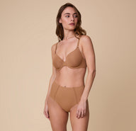 Gracie wears the No-Show Highwaist Brief in Tan, paired with the matching Base T-Shirt Bra, standing against a neutral background with a relaxed expression.