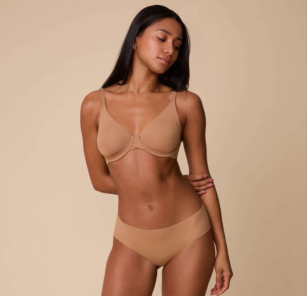 Ally wears the No-Show Hiphugger in Tan, paired with the matching Base Unlined bra, standing against a neutral background with a soft, confident expression.