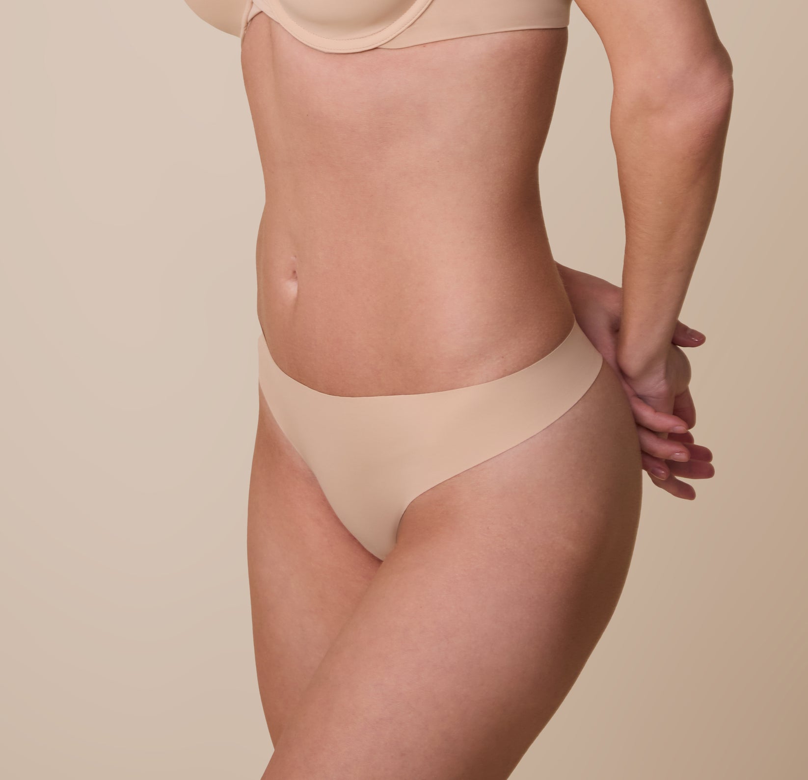 Gracie modeling the No-Show Thong in Beige at a three quarter angle.The soft, stretch fabric hugs her body for a barely-there feel.