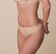 Gracie modeling the No-Show Thong in Beige at a three quarter angle.The soft, stretch fabric hugs her body for a barely-there feel.