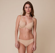 Gracie wearing the No-Show Thong in Beige, paired with a matching Base T-Shirt Bra. She poses with a soft smile, showcasing the thong’s flattering, seamless design.