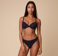 Ally wearing the No-Show Thong in Black paired with a matching Base T-Shirt Bra, standing against a neutral backdrop.