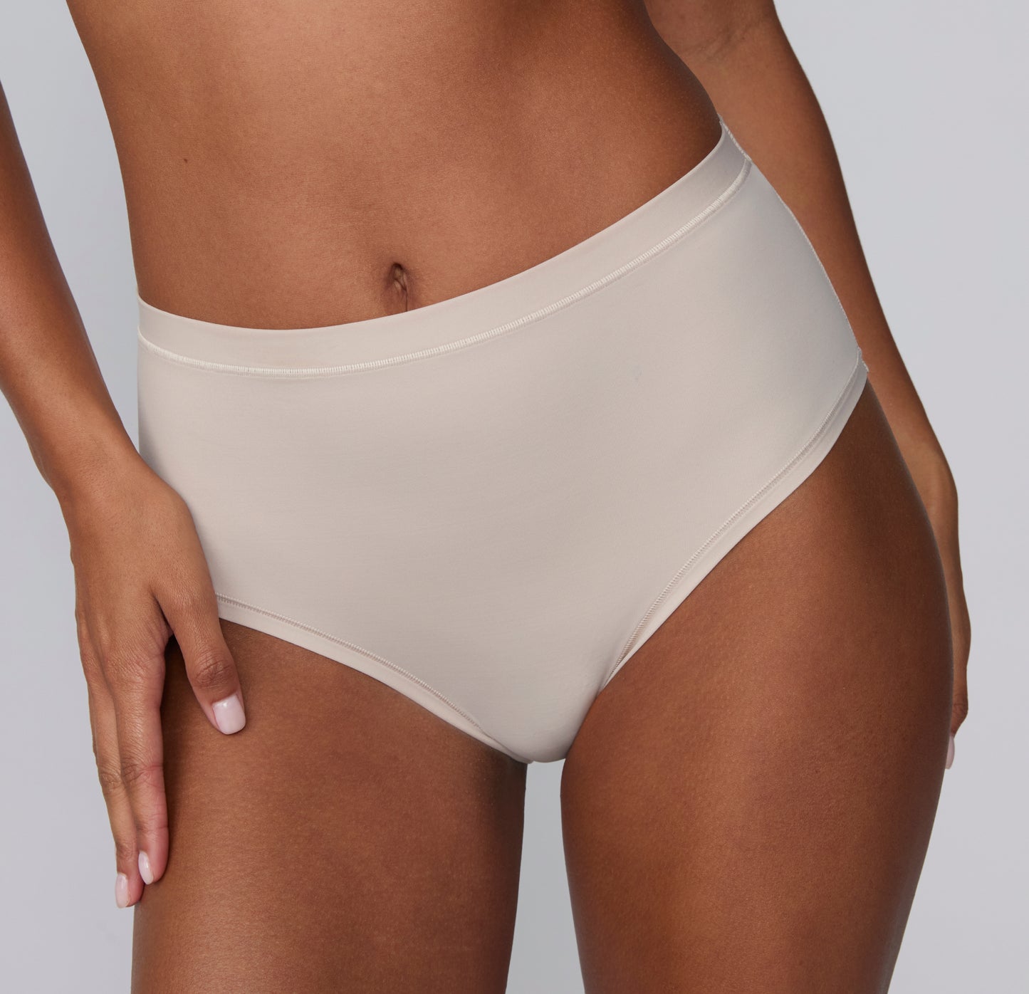 On a light gray studio backdrop, Courtney wears the Bliss Highwaist Brief in Pebble, shown in a close-up front view highlighting the smooth microfiber fabric, high-rise waist, and clean, no-show edges. sizing: Courtney wears size Small
