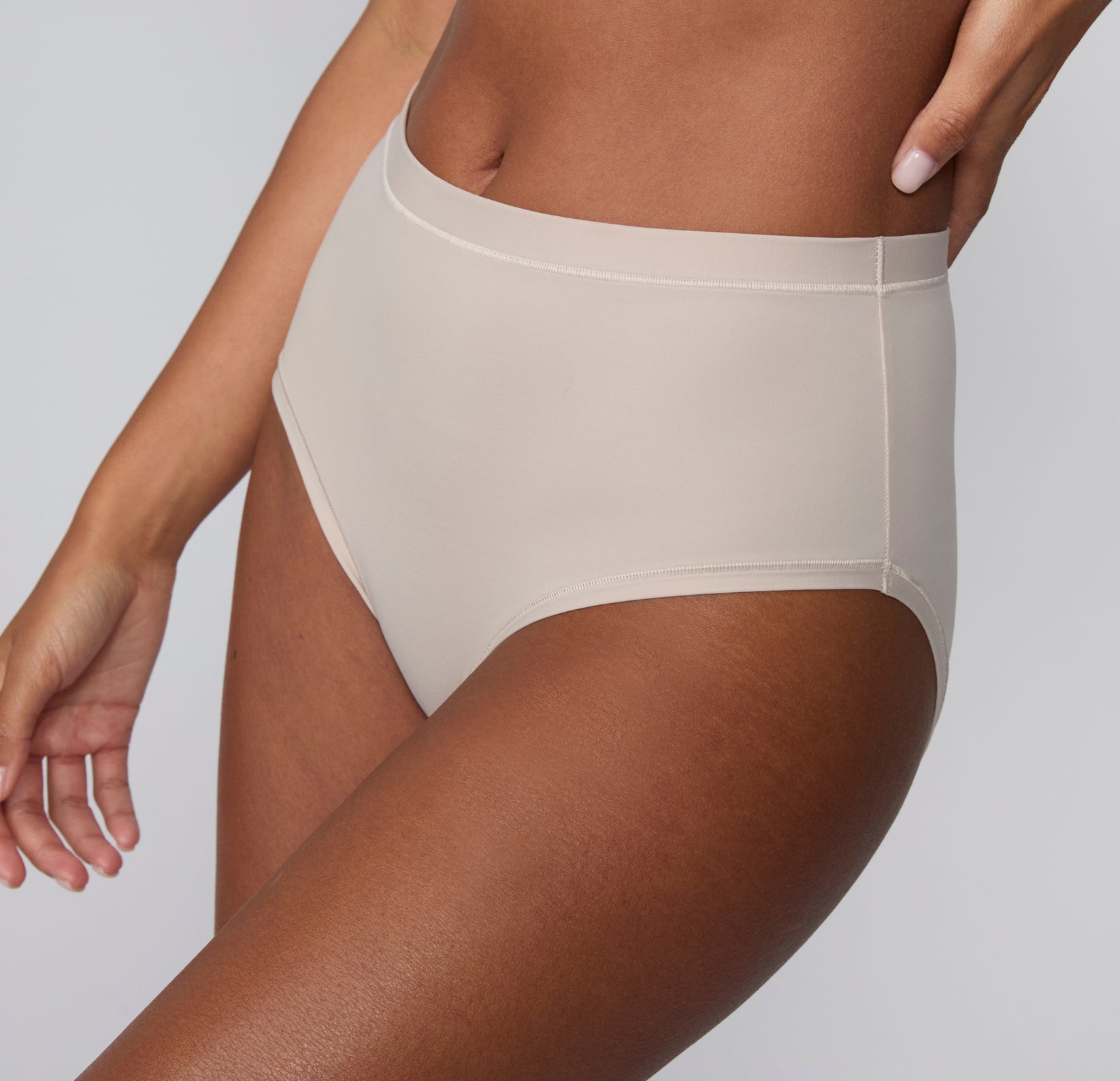 On a light gray studio backdrop, Courtney wears the Bliss Highwaist Brief in Pebble, shown in a three-quarter side view highlighting the high-rise waist, smooth microfiber fabric, and clean side seam.