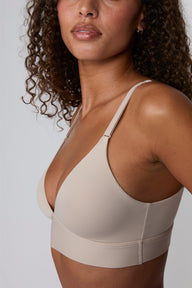 Close-up side view against a light grey backdrop, Courtney wears the Bliss Triangle Bralette in Pebble, highlighting the deep V neckline, smooth microfiber fabric, and wide wireless band.