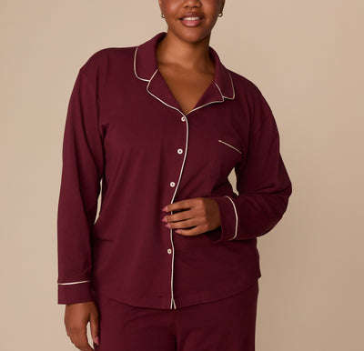 Front view of model Zarria wearing the Perfect Pima Long Sleeve Pajama Shirt and Pants in Bordeaux. The top features white contrast piping along the collar, button placket, and chest pocket. sizing: Zarria wears size XL