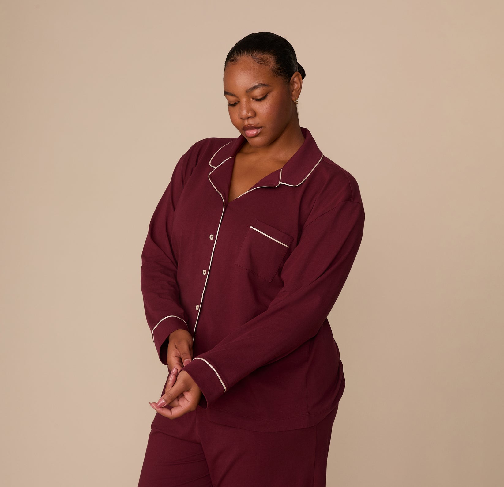Model Zarria wearing the Perfect Pima Long Sleeve Pajama Shirt in Bordeaux, adjusting the sleeve cuff. The chest pocket and button front are partially visible.