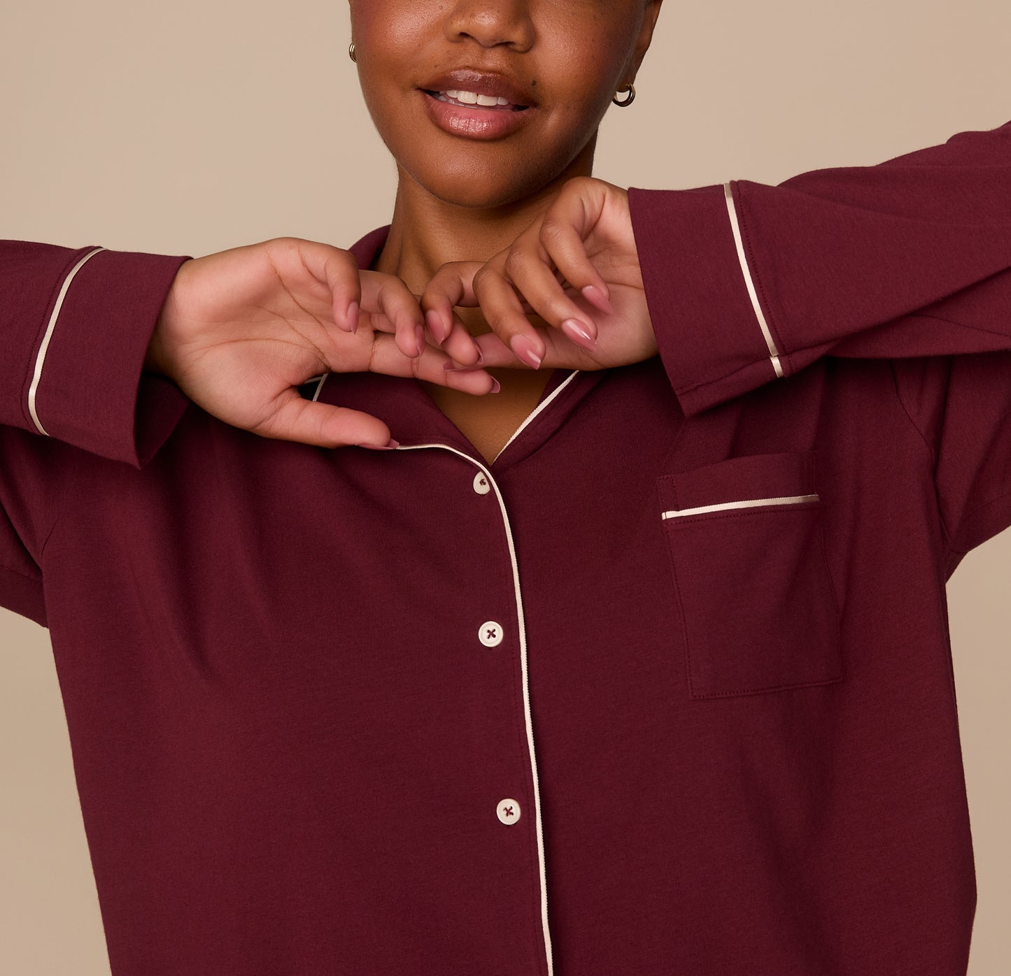 Partial close-up of model Zarria wearing the Perfect Pima Long Sleeve Pajama Shirt in Bordeaux. Her arms are raised near her face, showing the sleeve and front button detail.