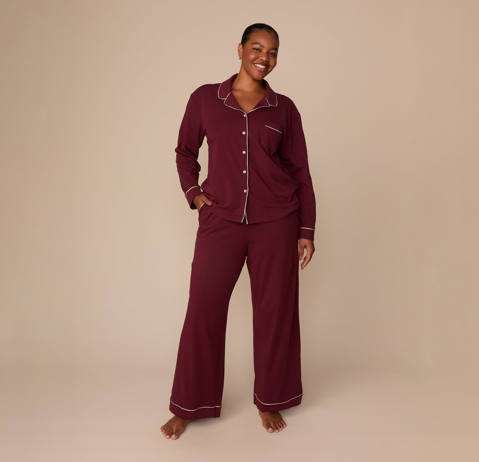 Full-body view of model Zarria wearing the Perfect Pima Long Sleeve Pajama Shirt and Pants in Bordeaux. She stands barefoot with one hand in her pocket, smiling softly.