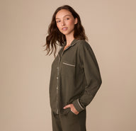 Side view of Alexis wearing the Perfect Pima Long Sleeve Pajama Shirt in Olive with her hands in her pockets. The full sleeve length and draped fit are visible.
