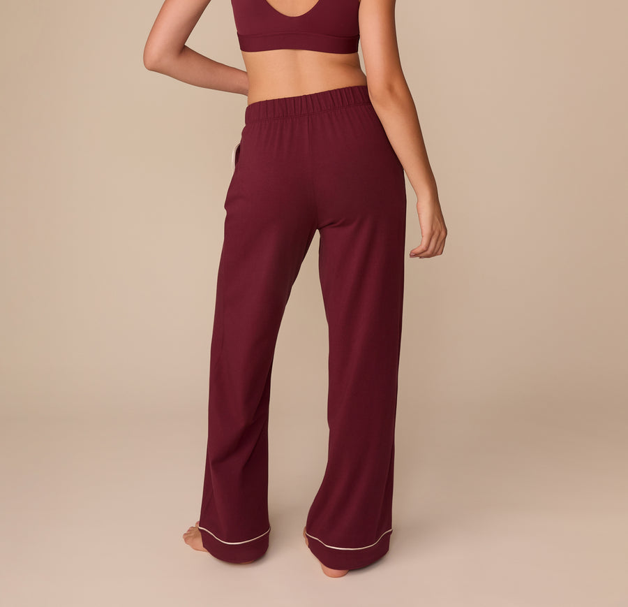 Back view of Alexis in the Perfect Pima Pajama Pants in Bordeaux. The wide-leg style and elastic waistband are shown from the rear, highlighting the soft drape of the fabric.