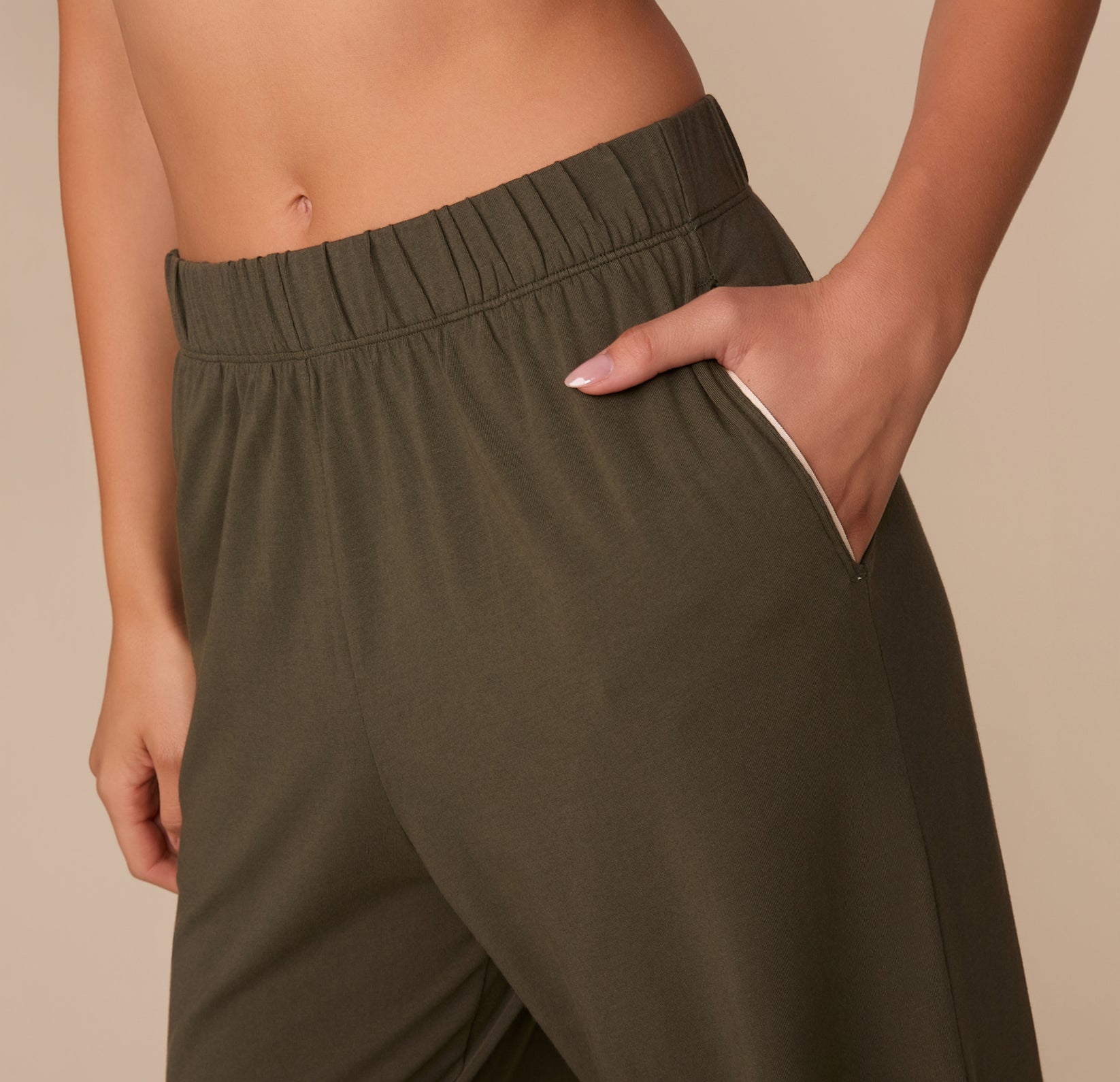 Close-up of Alexis’s hand in the pocket of the Perfect Pima Pajama Pants in Olive. The detail shows the soft elastic waistband and white piping on the pocket opening.