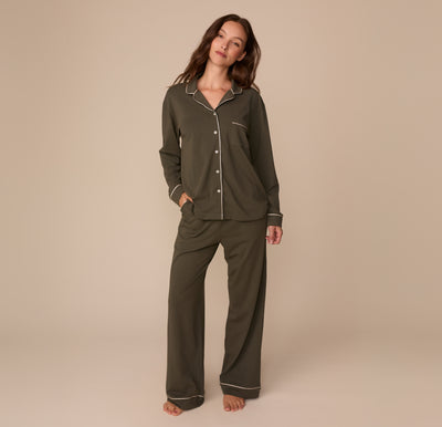 Full-body image of Alexis wearing the Perfect Pima Long Sleeve Pajama Shirt and Pajama Pants in Olive. She stands barefoot with hands in her pockets, showcasing the full matching pajama set.