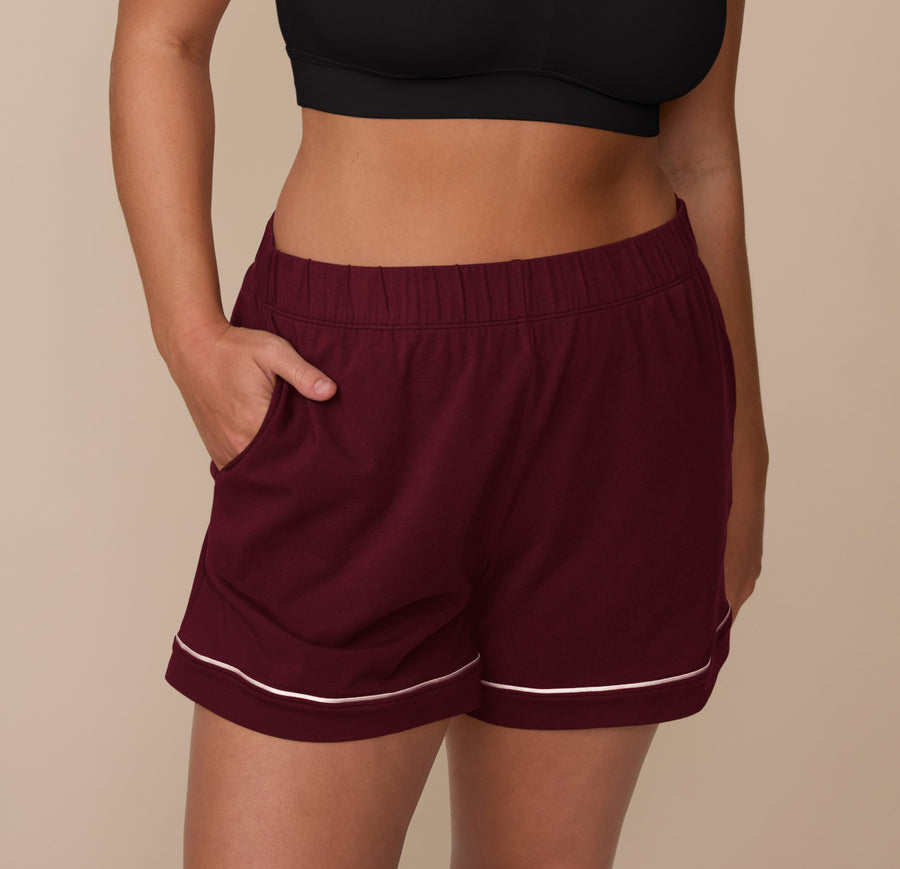 Close-up of model Sonnie wearing the Perfect Pima Pajama Shorts in Bordeaux. The shorts feature white contrast piping at the hem and an elastic waistband, with one hand in the pocket. sizing: Sonnie wears size Large