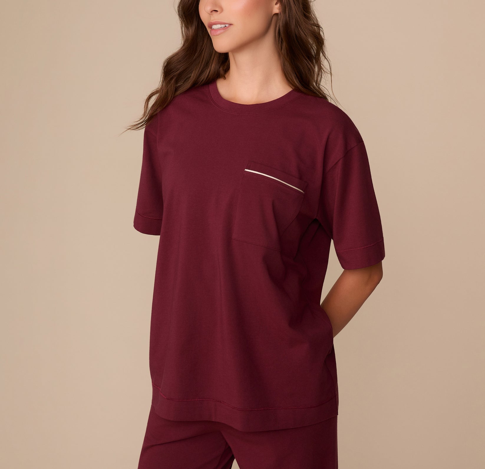 Side view of Alexis wearing the Perfect Pima Pajama Tee in Bordeaux. Her hands are tucked into her pants pockets, showcasing the drape of the tee.