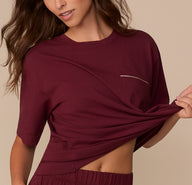 Model Alexis slightly lifts the hem of the Perfect Pima Pajama Tee in Bordeaux, revealing the elastic waistband of the coordinating pants.