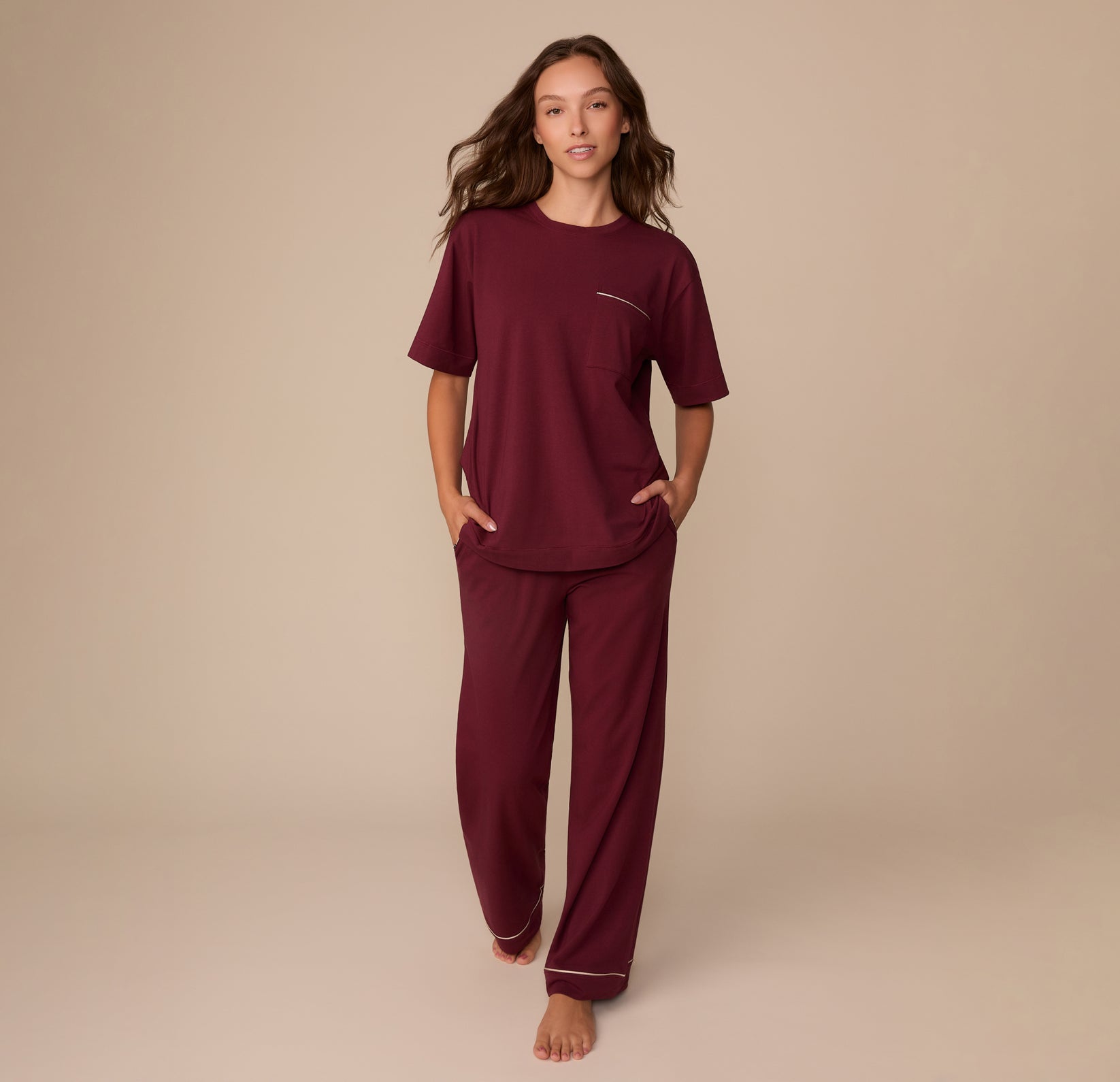 Full-body view of Alexis wearing the Perfect Pima Pajama Tee and Pants in Bordeaux. She walks barefoot with hands in her pockets, showcasing the soft, relaxed fit of the set.