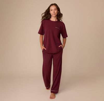 Full-body view of Alexis wearing the Perfect Pima Pajama Tee and Pants in Bordeaux. She walks barefoot with hands in her pockets, showcasing the soft, relaxed fit of the set.