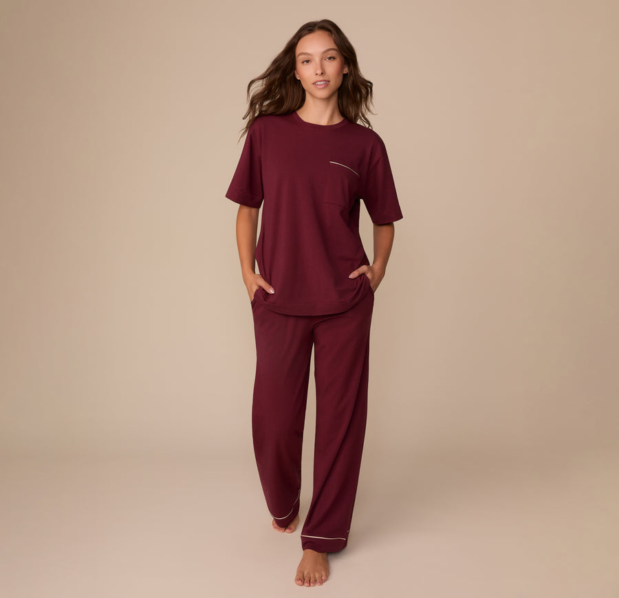 Full-body view of Alexis wearing the Perfect Pima Pajama Tee and Pants in Bordeaux. She walks barefoot with hands in her pockets, showcasing the soft, relaxed fit of the set.