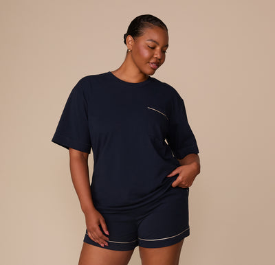 Zarria models the full pajama set, including the navy tee and shorts with matching ivory piping. Her pose is relaxed, emphasizing the comfort and easy fit of the set.