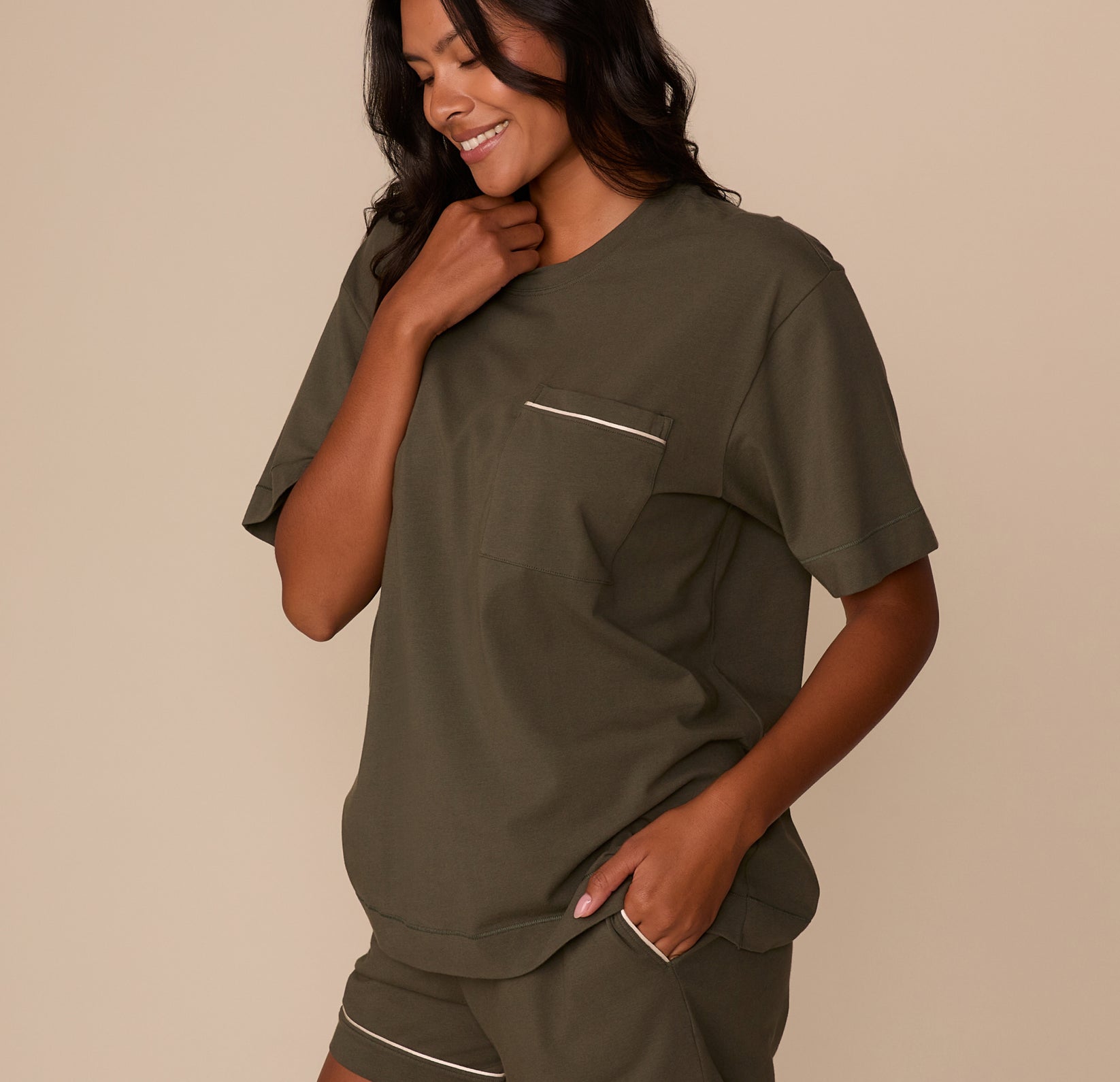 Side angle of Victoria wearing the Perfect Pima Pajama Tee and Shorts in Olive. She smiles with one hand on her collar and the other in her pocket, showing the soft, easy fit.