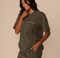 Side angle of Victoria wearing the Perfect Pima Pajama Tee and Shorts in Olive. She smiles with one hand on her collar and the other in her pocket, showing the soft, easy fit.