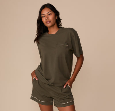 Full-body view of Victoria wearing the Perfect Pima Pajama Tee and Shorts in Olive. Both hands are in her pockets, showing off the comfy, coordinated sleep set.