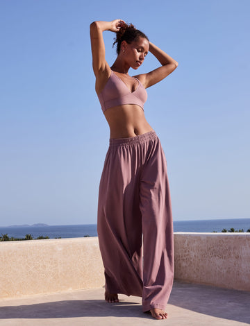 On a sunlit terrace overlooking the ocean, Courtney wears the Pima Palazzo Pant in Mirage with a matching wireless bra, showing the relaxed wide-leg silhouette, elastic waistband, and soft drape.