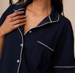 Close-up of the Perfect Pima Pajama Shirt in Navy, showing white contrast piping along the collar and pocket as Marcela gently touches the shirt.