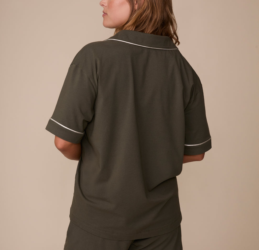 Back view of Sonnie wearing the Perfect Pima Pajama Shirt in Olive, highlighting the loose, comfortable fit and contrasting white piping detail across the back shoulders and sleeves.