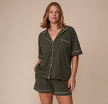 Full view of Sonnie wearing the matching Perfect Pima Pajama Shirt and Shorts in Olive, standing with hands in pockets and showcasing the relaxed, coordinated set with white trim details.
