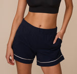 Close-up of Marcela wearing the Perfect Pima Pajama Shorts in Navy, featuring an elastic waistband, curved side pockets, and contrast white piping at the cuffed hem. sizing: Marcela wears size XS