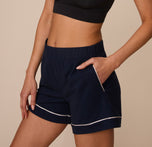 Side angle of Marcela in the Perfect Pima Pajama Shorts in Navy, with her hand in the pocket and the white piping highlighting the shape of the cuff and pocket opening.
