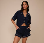 Marcela wears the matching pajama set in Navy, including the Perfect Pima Pajama Shirt and Shorts, styled casually with the shirt partially unbuttoned and both hands in her shorts pockets.