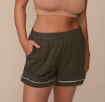 Close-up of Sonnie wearing the Perfect Pima Pajama Shorts in Olive, showcasing the elastic waistband, functional side pockets, and white piping at the cuffed hem. sizing: Sonnie wears size Large