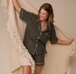 Sonnie wears the full Olive pajama set while playfully wrapped in a soft, cream woven blanket, showing the pajama shorts’ relaxed fit and contrast piping.
