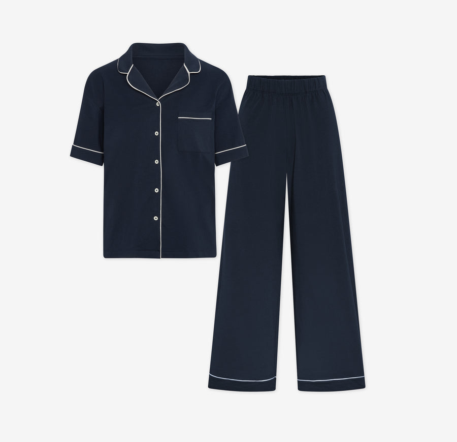 Harper Wilde Pima Pajama Set in Navy. Includes short sleeve, button-up top with white piping and matching long pajama pants. Set laid flat on a white background.