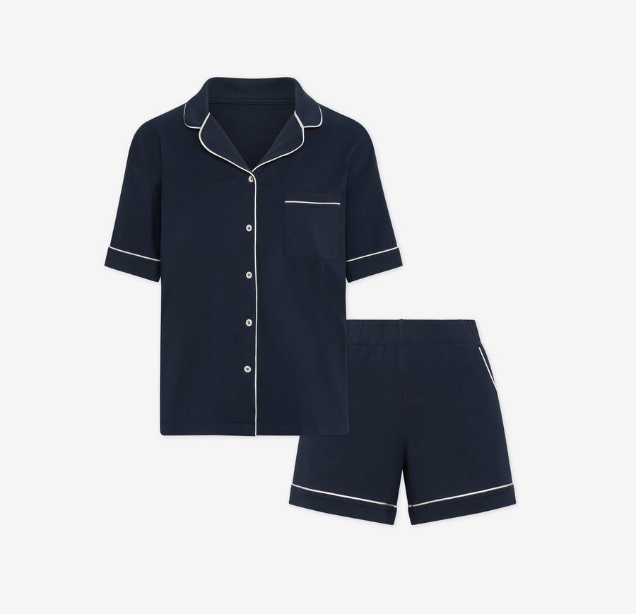 Harper Wilde Pima Pajama Set in Navy. Includes short sleeve, button-up top with white piping and matching pajama shorts. Set laid flat on a white background.