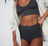 On a clean studio backdrop, a model wears the Ribbed Boyshort in Charcoal, shown from the front with a wide, ribbed waistband and soft, stretchy fabric.