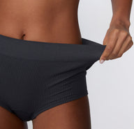 Close-up on a model wearing the Ribbed Boyshort in Charcoal, pulling the waistband slightly to show the stretchy ribbed fabric and flexible fit.