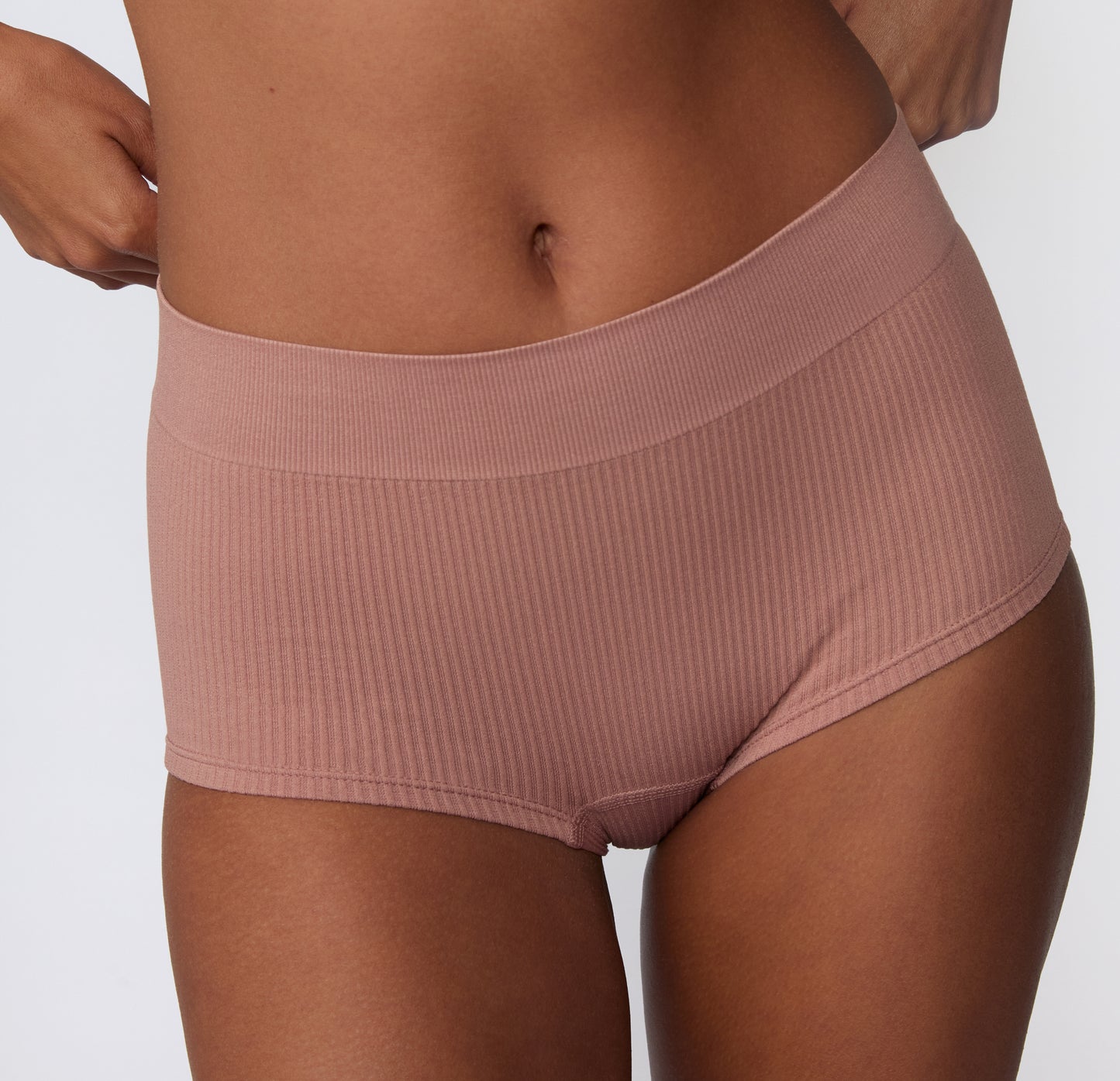 On a light studio backdrop, a model wears the Ribbed Boyshort in Plum, shown from the front with a wide waistband and soft ribbed fabric.