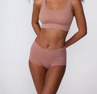 On a clean studio background, a model wears the Ribbed Boyshort in Plum paired with a matching ribbed bralette, showing the full set from the front.