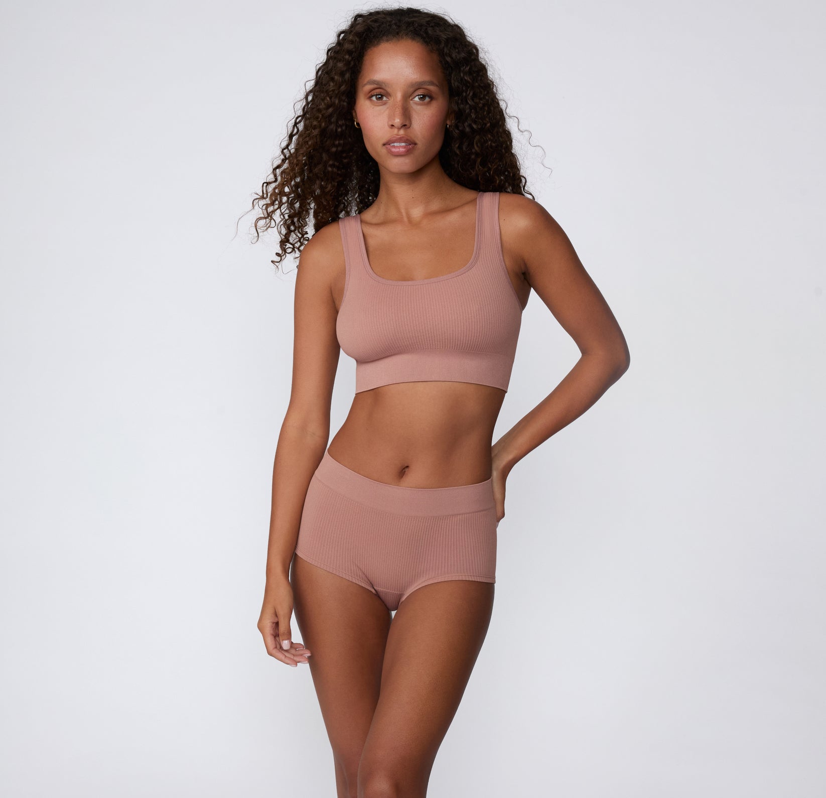 Full-body studio shot of a model wearing the Ribbed Boyshort in Plum with a coordinating ribbed bralette, highlighting the smooth waistband and ribbed texture.