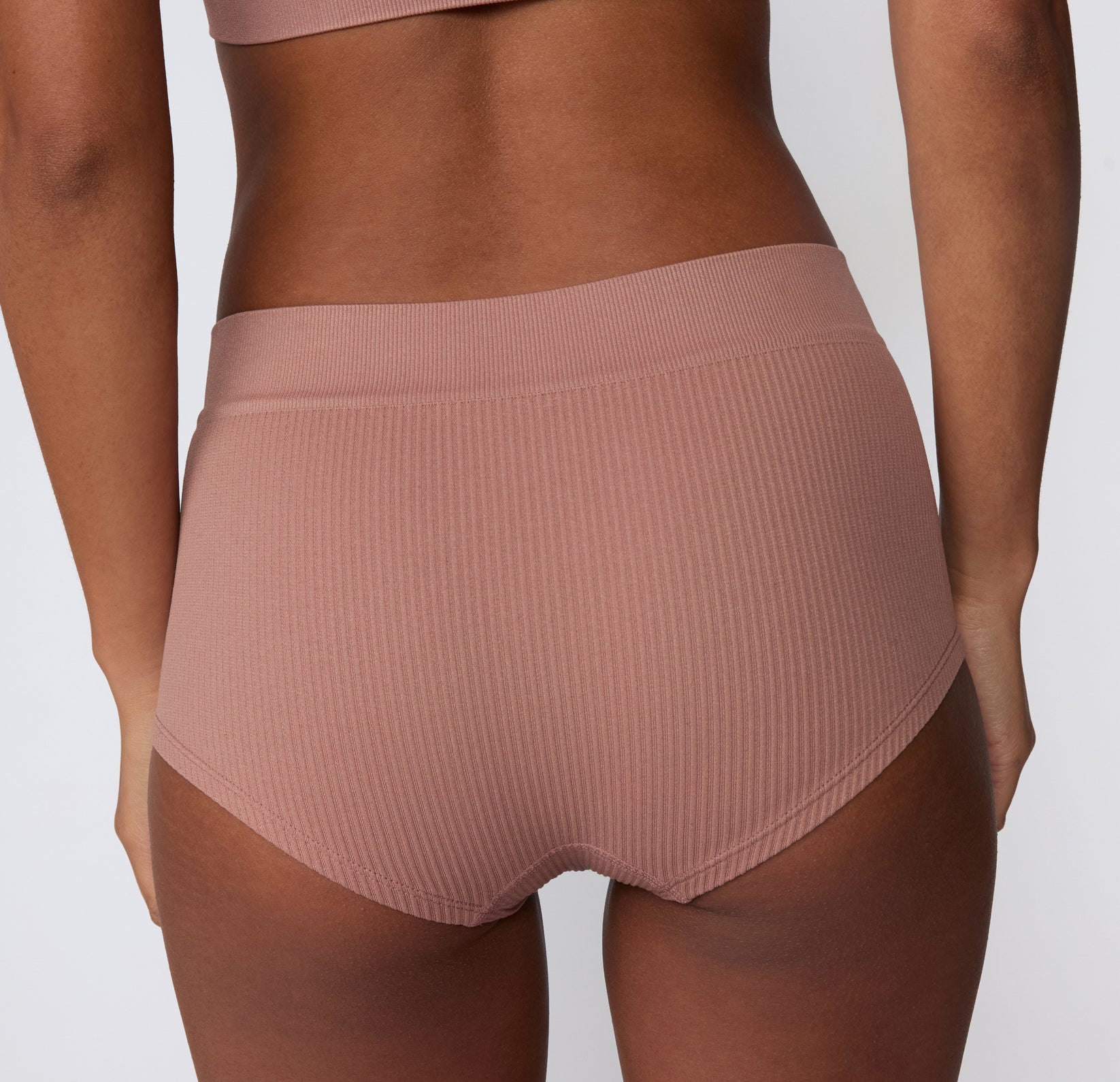 On a white studio backdrop, the Ribbed Boyshort in Plum is shown from the back, highlighting the ribbed texture, wide waistband, and comfortable, full-coverage fit.