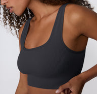 On a light studio backdrop, a close-up side view shows a model wearing the Ribbed Scoop Bralette in Charcoal, highlighting the soft ribbed fabric, scoop neckline, and wide straps designed for everyday comfort.