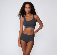 On a light studio backdrop, a full-body front view shows a model wearing the Ribbed Scoop Bralette and matching underwear in Charcoal, emphasizing the ribbed fabric and comfortable, wireless design.