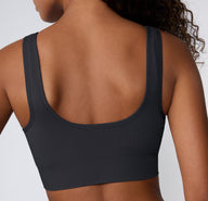 On a light studio backdrop, a back view shows a model wearing the Ribbed Scoop Bralette in Charcoal, highlighting the scoop back shape, wide straps, and smooth ribbed fabric.