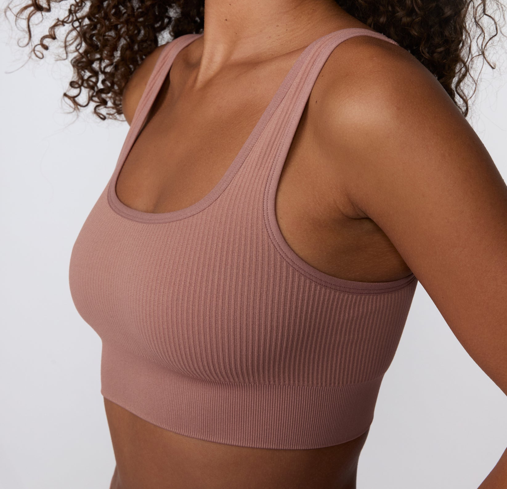 On a light studio backdrop, a close-up side view shows a model wearing the Ribbed Scoop Bralette in Plum, focusing on the ribbed texture, wide straps, and smooth underband for everyday comfort.