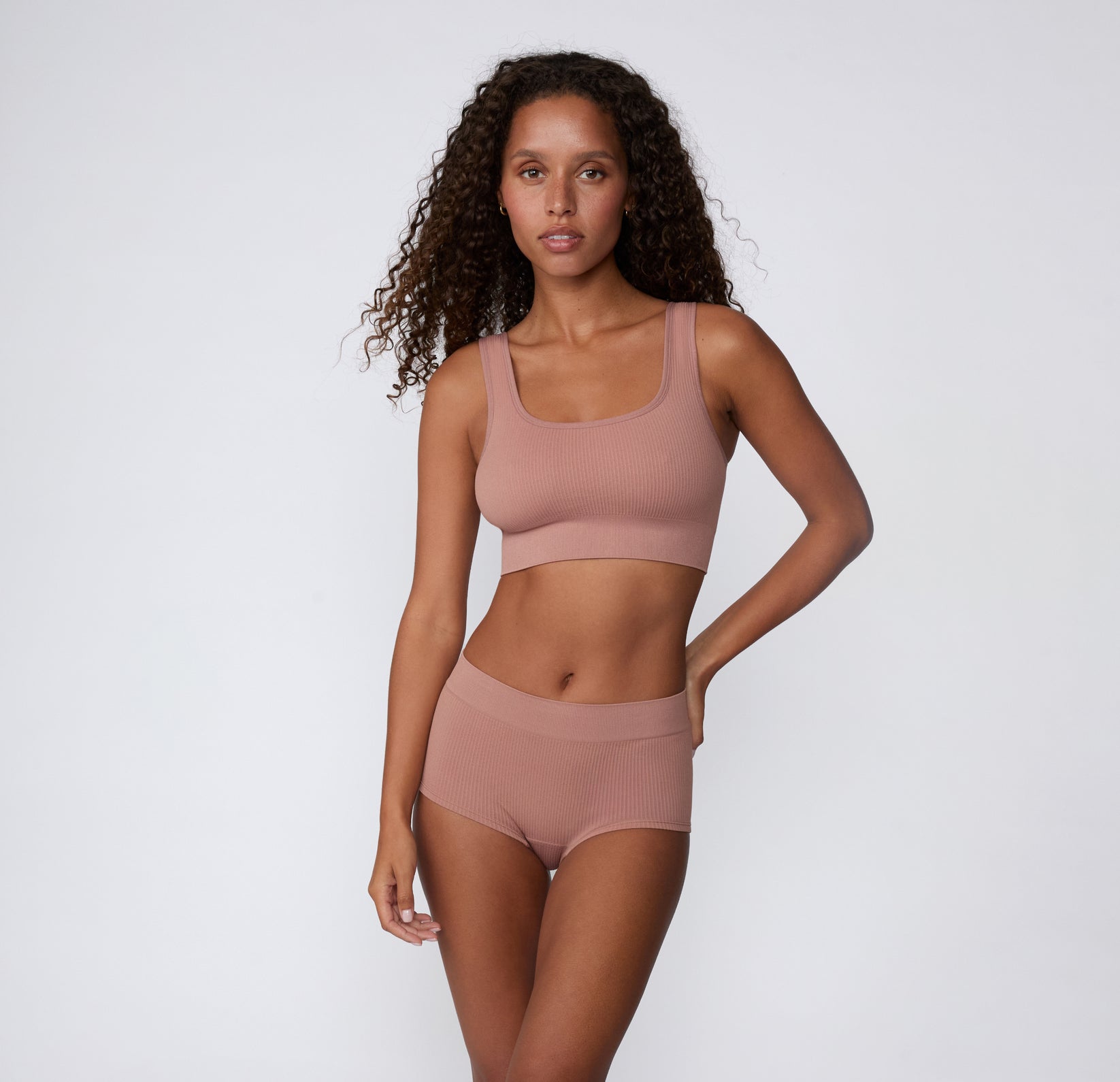 On a light studio backdrop, a full-body front view shows a model wearing the Ribbed Scoop Bralette and matching underwear in Plum, emphasizing the ribbed fabric and comfortable, wireless design.